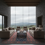 A modern living room with two beige sofas, two armchairs, a black coffee table, and a red and blue patterned rug, set against a backdrop of stone walls and a large window overlooking a mountain landscape.