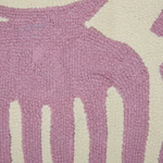 A close-up of a textured, looped pile rug featuring a large dusty pink abstract shape over an off-white background.