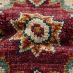 Close-up of a textured area rug with a traditional geometric pattern in deep red, cream, mustard yellow, and navy blue.
