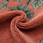 Close-up of a plush, dusty rose rug with a textured, shaggy pile and a green floral pattern.