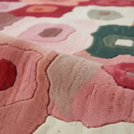 A close-up of a plush, textured area rug featuring a retro concentric circle pattern in shades of pink, dusty rose, cream, and sage green.