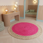 A round area rug with a bright pink center and a natural beige braided border, placed on a light wood floor in a modern, whimsical children's room.