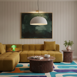 A modern living room scene featuring a mustard yellow sectional sofa, a round marble-top coffee table, a ribbed side table with a plant, and a large abstract painting on a paneled wall.