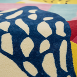 Close-up of a colorful area rug with a dark navy blue abstract leaf-like pattern over a cream base, with other visible colors including pink, light blue, red, and yellow.