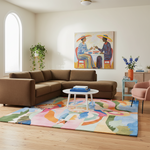 A styled living room featuring a large brown sectional sofa, a colorful abstract area rug, a white coffee table, and a framed painting on the wall.