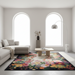 A large rectangular area rug with a dense multicolor floral print lies on a light floor in a bright, modern living room. The room features a light beige sectional sofa, a low wooden coffee table, a marble side pedestal with a vase of branches, and a silver floor lamp, all set against two tall arched windows.