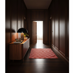 A red and pink checkerboard area rug lies on a dark wood hallway floor next to a wooden console table with a lit black table lamp.