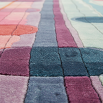 A close-up of a plush area rug with a colorful geometric patchwork design in shades of pink, blue, purple, and gray.