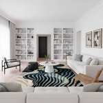 A modern living room with a large abstract wavy area rug in black, navy, teal, and beige, styled with a white sofa, white armchair, and built-in white bookshelves.