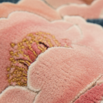 Close-up of a plush, textured pink floral rug with gold and red embroidered details.