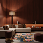 A modern living room scene with a cream sectional sofa, brown leather and patterned throw pillows, a floral area rug, a floor lamp, and warm wood-paneled walls.