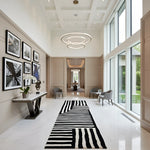 Modern interior hallway with a black and white striped rug, wall art, and large windows.