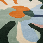 Close-up of a plush area rug with an abstract, organic floral pattern in shades of light blue, sage green, dark forest green, cream, and orange.