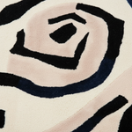 A close-up of a plush area rug with a modern abstract pattern featuring a large spiral in black, cream, blush pink, and dark navy blue.