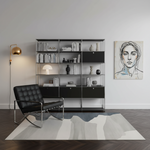 A modern black leather armchair with a chrome frame sits on a large abstract-patterned area rug in a minimalist living room. Behind the chair is a tall black metal shelving unit filled with books and decor, and to the right is a framed portrait painting on the wall.