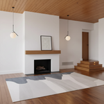A large abstract area rug in white, gray, and light taupe tones, styled in a modern minimalist living room with a wood fireplace, white walls, and wood flooring.