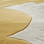 Close-up of a plush area rug with a stylized abstract design in mustard yellow and off-white, showing the soft pile texture and curved seam details.