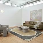 A modern living room with a green leather sofa, two round gray coffee tables, a large patterned area rug, a gray armchair, and a large abstract painting on the wall.