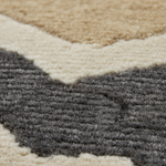 Close-up of a textured area rug with a geometric chevron pattern in charcoal gray, cream, and tan.