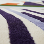 Close-up of a plush textured rug with bold diagonal stripes in deep purple, light lavender, and off-white.