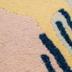 Close-up of a textured area rug with a modern abstract design in dusty pink, pale yellow, navy blue, and light gray.