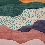 Close-up of a plush area rug with an abstract, wavy landscape design in multiple colors including teal, cream with teal spots, dusty pink, purple, and peach.