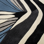 Close-up of a textured area rug with a modern abstract design featuring bold black, cream, blue, and gray curved stripes.