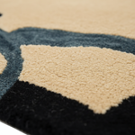 Close-up of a textured area rug with a modern abstract pattern in beige, slate blue, and black.