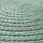A close-up of a round braided rug in a muted sage green color, showing the detailed texture of the woven fibers.