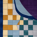 A close-up of a geometric patterned textile or rug featuring a checkerboard grid in cream, mustard, light blue, teal, and gray, overlaid with a large curved shape in dark blue and a purple section.