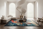 A large rectangular area rug with an abstract geometric cityscape pattern in blue, teal, orange, beige, and gray, styled in a bright, modern living room with a spiral staircase, white sectional sofa, and wood flooring.