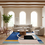A modern living room with a large abstract area rug in blue, beige, yellow, and black, styled with a cream sofa, wooden coffee table, armchair, and a potted plant.
