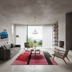 A modern living room with a large abstract area rug in pink, red, and green tones, styled with a gray sofa, wooden chairs, a concrete ceiling, and a large window overlooking a distant landscape.