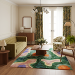 A styled living room featuring a large abstract area rug with green, pink, orange, and blue organic shapes on a wood floor. The room includes a green ribbed sofa, a floral armchair, a wooden coffee table, and green patterned curtains.