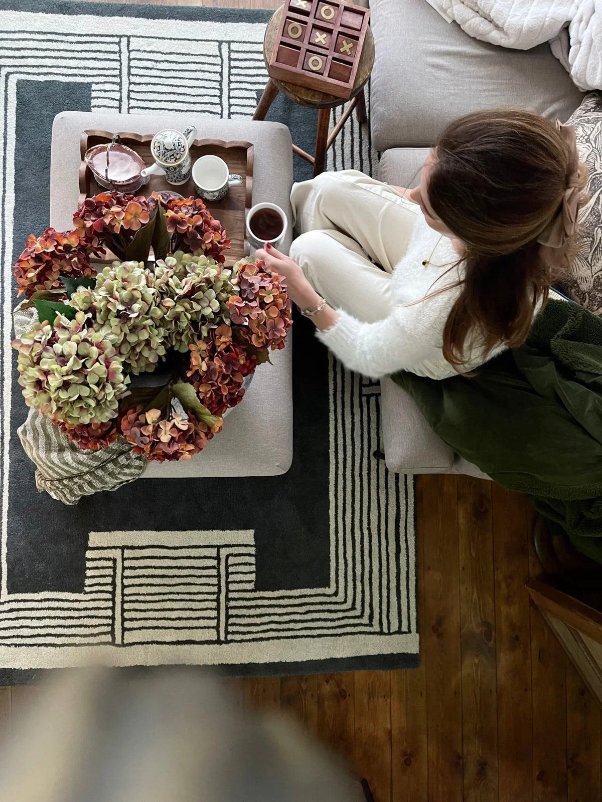 Person sitting on a couch next to a coffee table with a large floral arrangement.