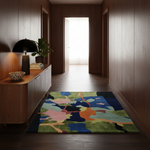 A colorful abstract area rug with green, blue, pink, and orange shapes, placed on a dark wood floor in a modern hallway with wood-paneled walls.