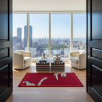 A red rectangular area rug with black and white leopard print motifs is styled in a modern living room setting with two cream armchairs and a striped coffee table, set against a large window overlooking a city skyline.