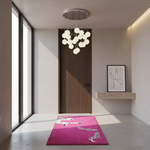 A modern interior hallway with a bright pink rectangular rug featuring white zebra prints, placed on a light concrete floor in front of a dark wood door. A chandelier hangs above, and a small shelf with framed abstract art is on the right.