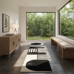 A modern minimalist entryway with a long black and cream abstract runner rug on dark tile flooring, flanked by a light wood sideboard on the left and a matching wooden bench by large windows looking out to a green garden.