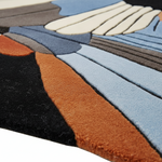 Close-up of a textured area rug with an abstract, layered geometric pattern in shades of blue, rust orange, black, gray, and cream.