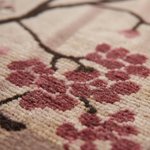 Close-up of a textured rug featuring a cherry blossom pattern with dusty pink flowers and dark brown branches on a warm cream background.